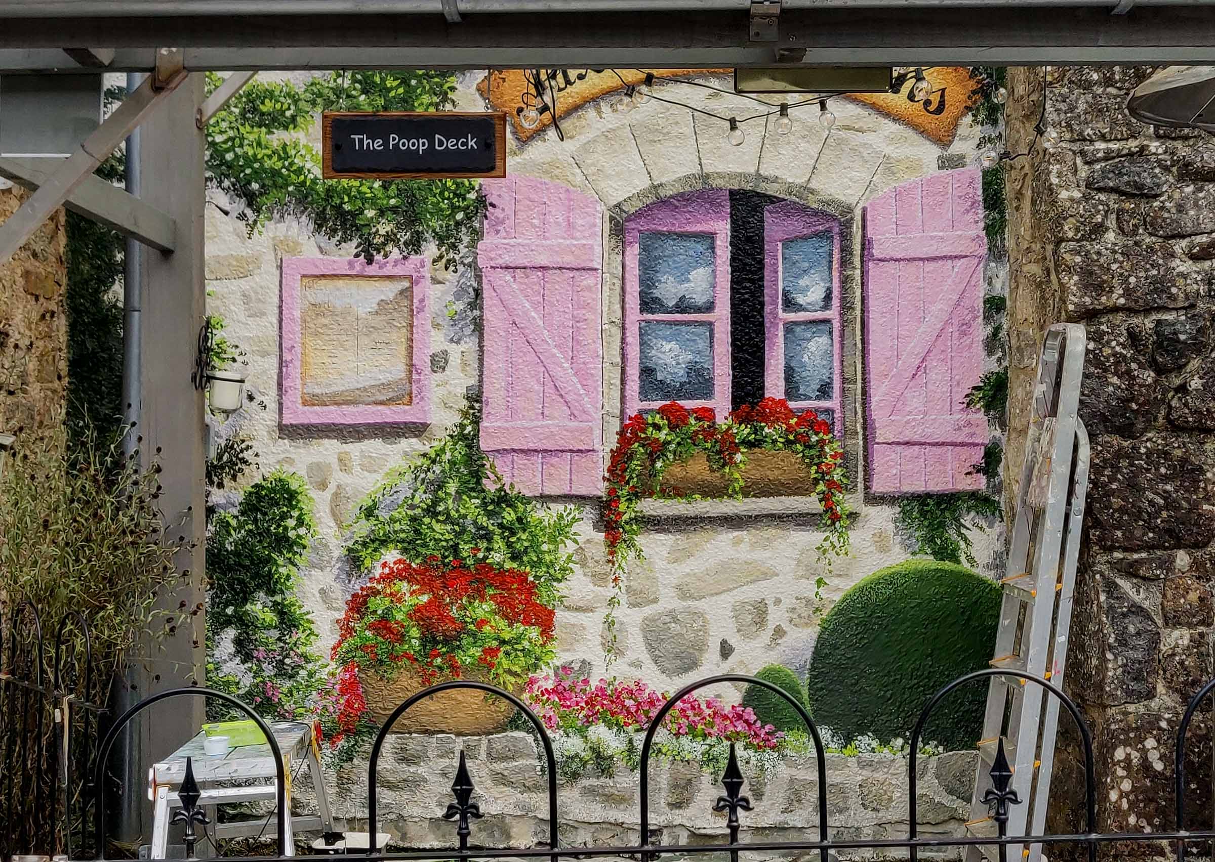 Troughs of bountiful flowering plants are spilling over hand painted stonework